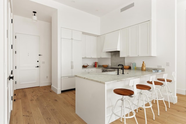 kitchen featuring a breakfast bar area, light wood-type flooring, a peninsula, custom range hood, and white cabinetry