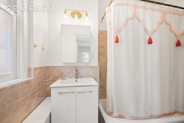 full bath featuring tile walls, shower / bath combo, vanity, and a wainscoted wall