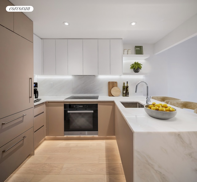 kitchen with black oven, modern cabinets, a sink, light countertops, and recessed lighting