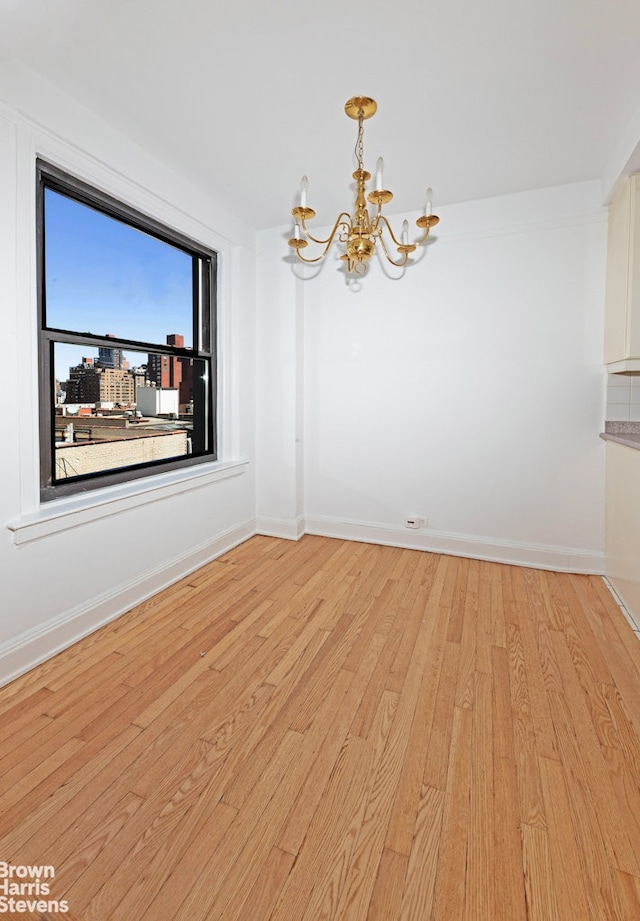 unfurnished dining area featuring baseboards, light wood finished floors, and a notable chandelier
