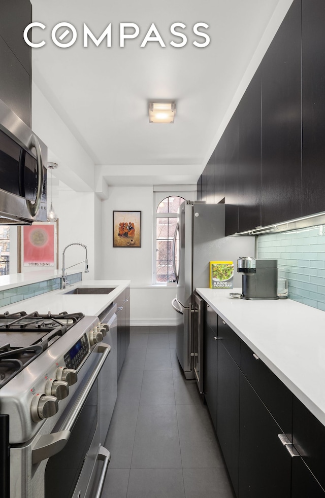 470 W 24th St Unit 2C, New York City, NY 10011 - kitchen with appliances with stainless steel finishes, dark cabinetry, a sink, decorative backsplash, and light countertops