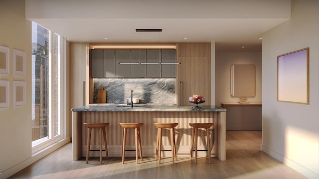 499 9th Ave Unit 9Dn, New York City, NY 10018 - kitchen featuring light wood-style floors, decorative backsplash, a kitchen breakfast bar, a sink, and gray cabinets