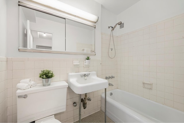 bathroom with tile walls, bathtub / shower combination, a sink, toilet, and wainscoting