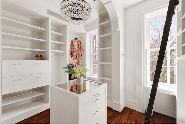 spacious closet with arched walkways, a notable chandelier, and dark wood-style flooring