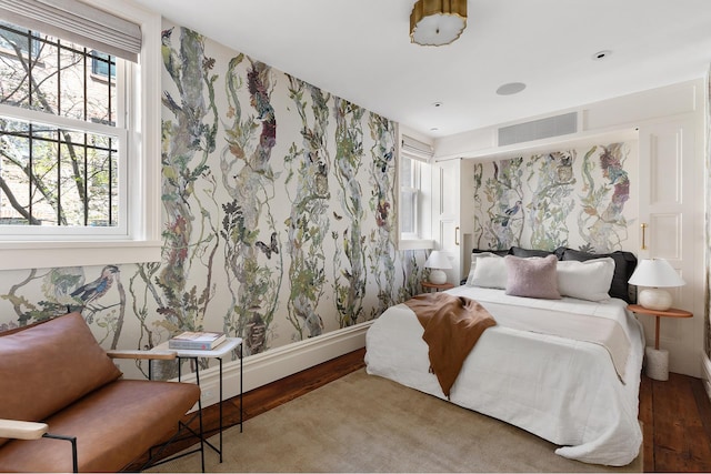 bedroom with wallpapered walls, wood finished floors, visible vents, and multiple windows