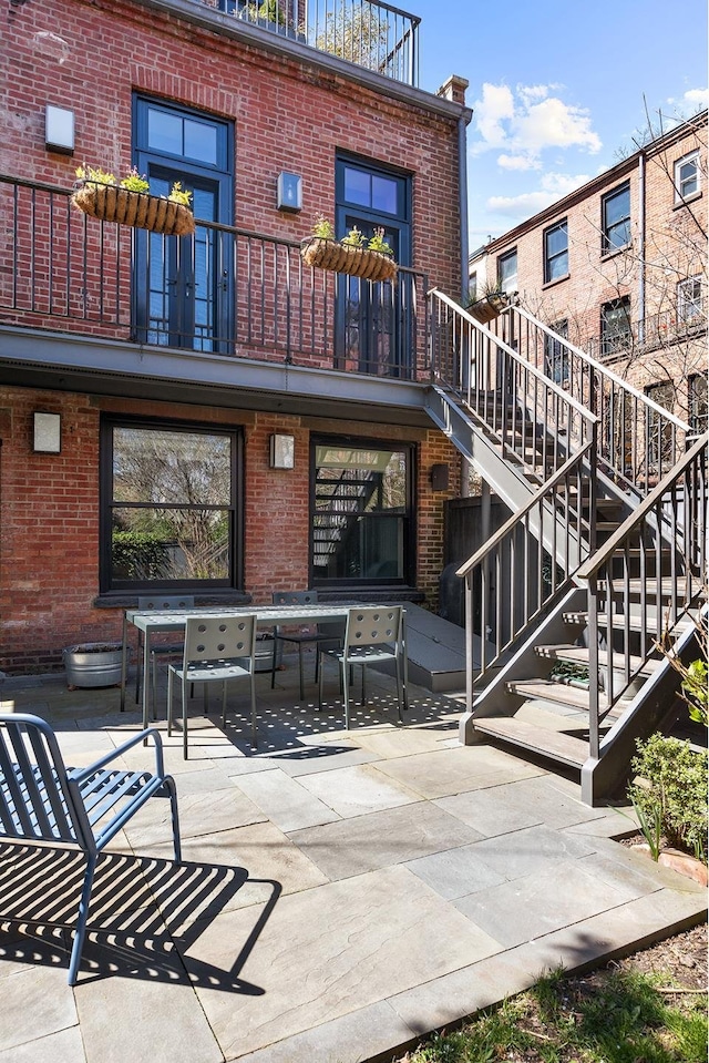 back of house featuring brick siding, a patio area, stairway, and a balcony