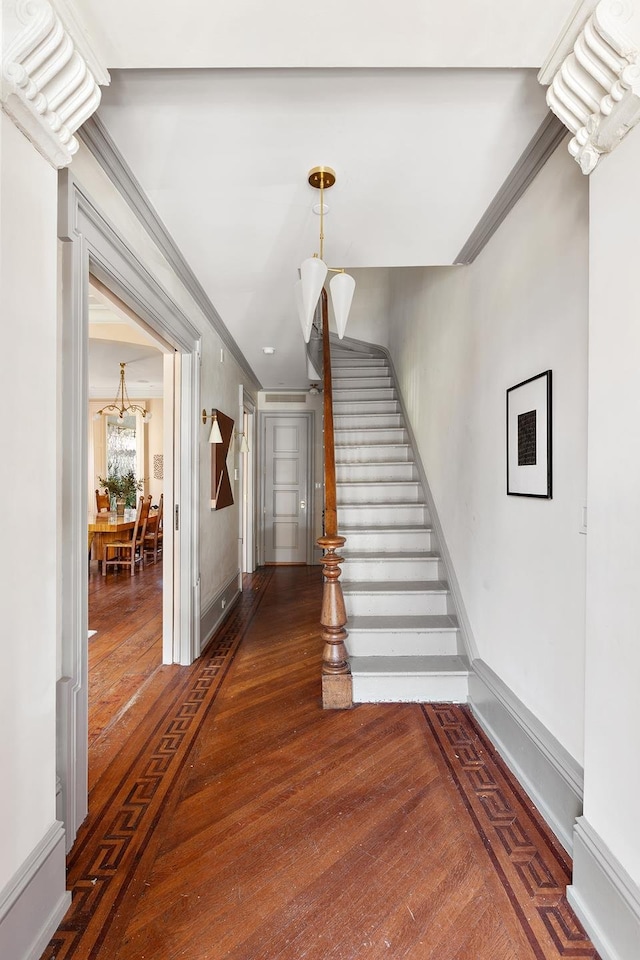 staircase with hardwood / wood-style floors, baseboards, a notable chandelier, and ornamental molding