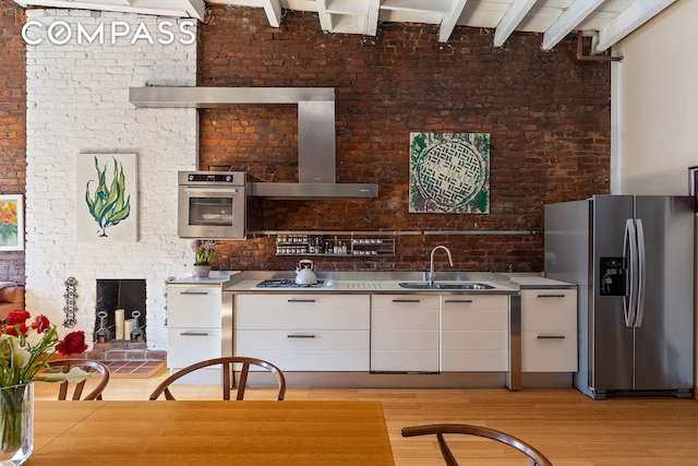 kitchen with brick wall, a sink, white cabinets, light wood finished floors, and stainless steel appliances