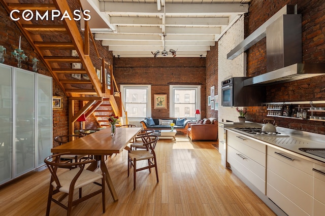 138 Lexington Ave Ph, Ph, New York City, NY 10016 - kitchen with brick wall, stainless steel gas cooktop, a high ceiling, wall chimney range hood, and light wood-style floors