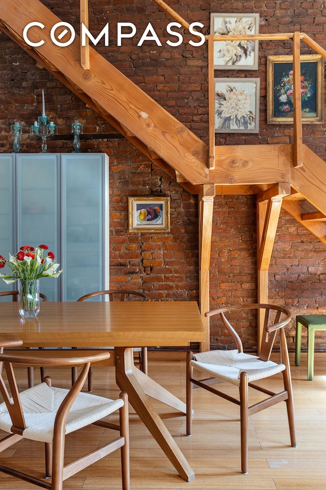 dining room featuring wood finished floors, brick wall, and vaulted ceiling