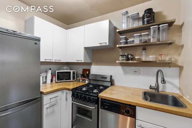 kitchen with white cabinets, a sink, wood counters, stainless steel appliances, and backsplash