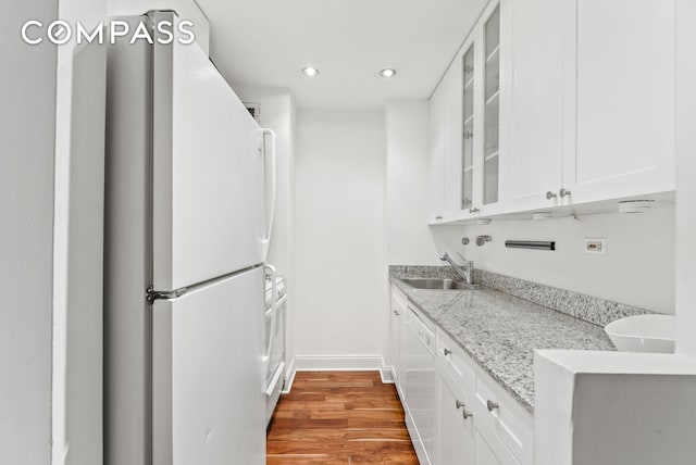 kitchen featuring recessed lighting, white appliances, wood finished floors, glass insert cabinets, and baseboards