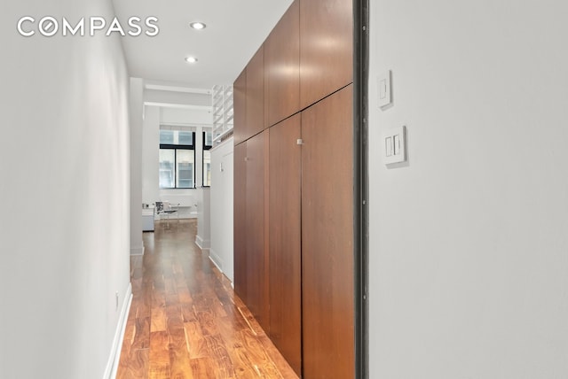 corridor featuring light wood-type flooring, recessed lighting, and baseboards