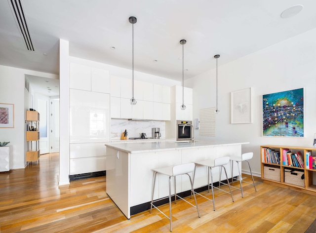 53 Warren St Unit 4, New York City, NY 10007 - kitchen featuring a breakfast bar area, light wood-type flooring, light countertops, tasteful backsplash, and white cabinetry