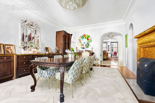 dining area featuring arched walkways, ornamental molding, a chandelier, and light wood-style floors