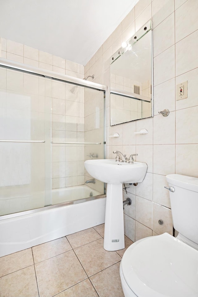 full bath with tile walls, toilet, bath / shower combo with glass door, and tile patterned flooring