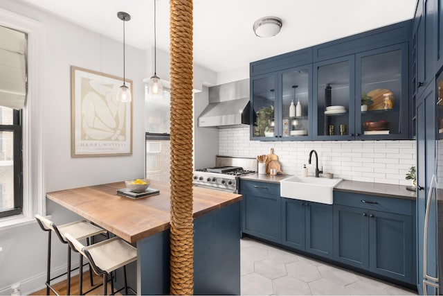kitchen with wall chimney exhaust hood, a sink, butcher block countertops, blue cabinets, and backsplash