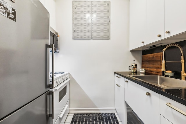 kitchen with white cabinets, dark countertops, a sink, stainless steel appliances, and baseboards