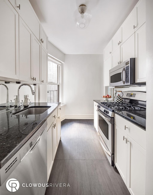 kitchen featuring appliances with stainless steel finishes, a sink, baseboards, white cabinetry, and dark stone countertops
