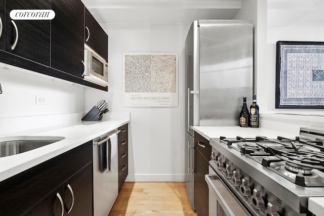 77 Bleecker St Unit 810, New York City, NY 10012 - kitchen with stainless steel appliances, light wood-style flooring, light countertops, baseboards, and dark cabinetry