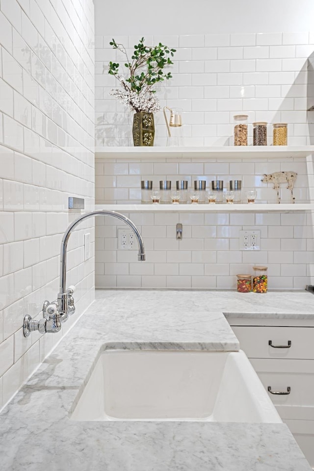 interior space with backsplash, light stone countertops, open shelves, a sink, and white cabinets