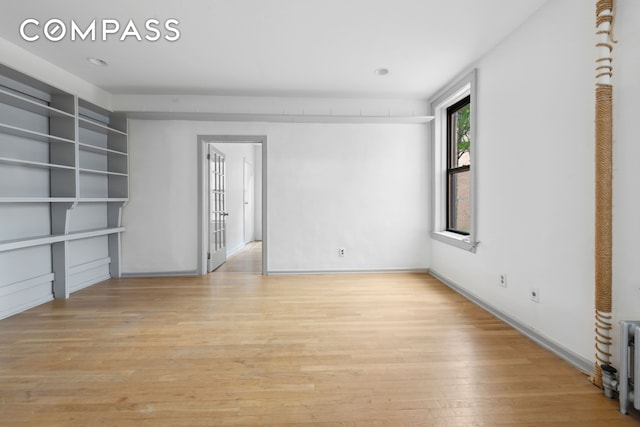 empty room featuring light wood-style flooring, built in shelves, and baseboards
