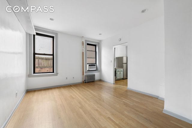 unfurnished living room featuring radiator heating unit, light wood-type flooring, baseboards, and cooling unit