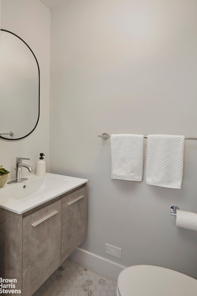 half bathroom with toilet, tile patterned floors, vanity, and baseboards