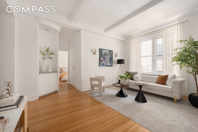 living area with light wood-type flooring, beamed ceiling, and baseboards