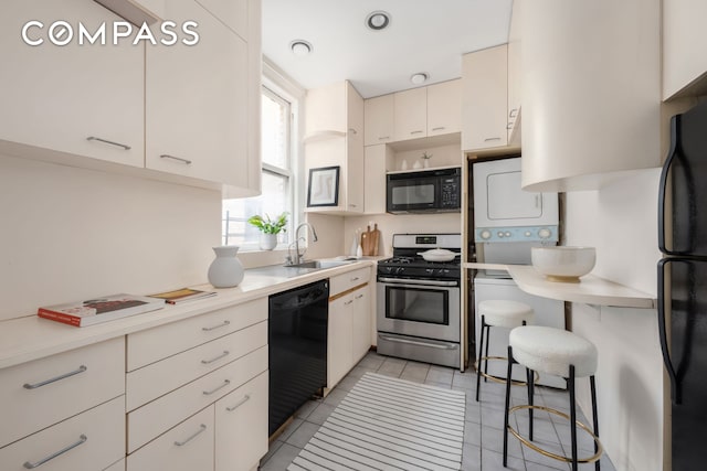 kitchen with black appliances, stacked washer / drying machine, a sink, light countertops, and light tile patterned floors