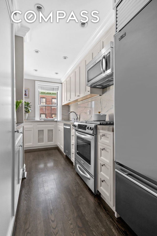 75 Bank St Unit 3K, New York City, NY 10014 - kitchen featuring stainless steel appliances, white cabinets, dark wood finished floors, decorative backsplash, and crown molding