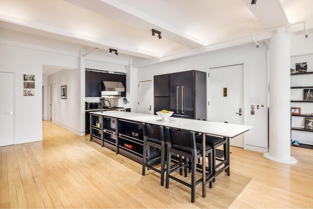 kitchen with high end black fridge, wall chimney range hood, dark cabinetry, and light wood-type flooring