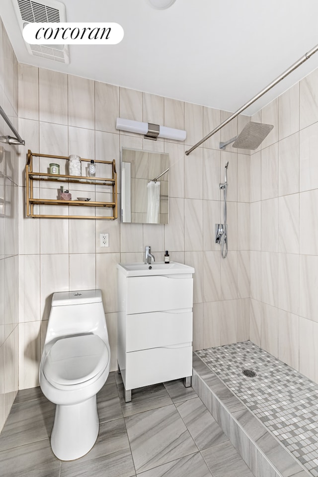bathroom with tile walls, tiled shower, toilet, and vanity