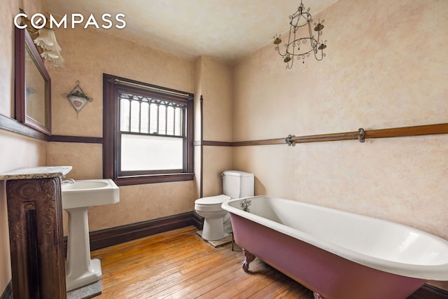 bathroom featuring a soaking tub, hardwood / wood-style flooring, and toilet