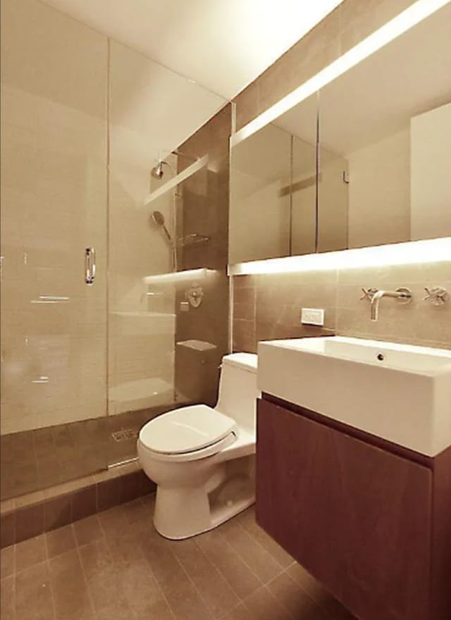 515 E 72nd St Unit 4B, New York City, NY 10021 - full bath featuring tile walls, a stall shower, toilet, vanity, and tile patterned floors