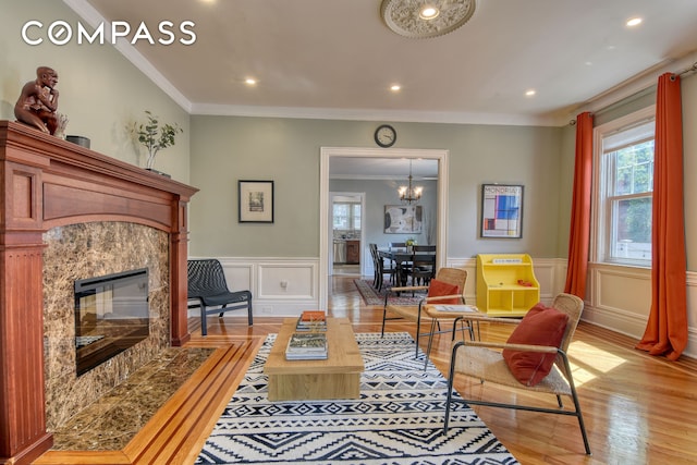 living area with wainscoting, a decorative wall, crown molding, and light wood finished floors