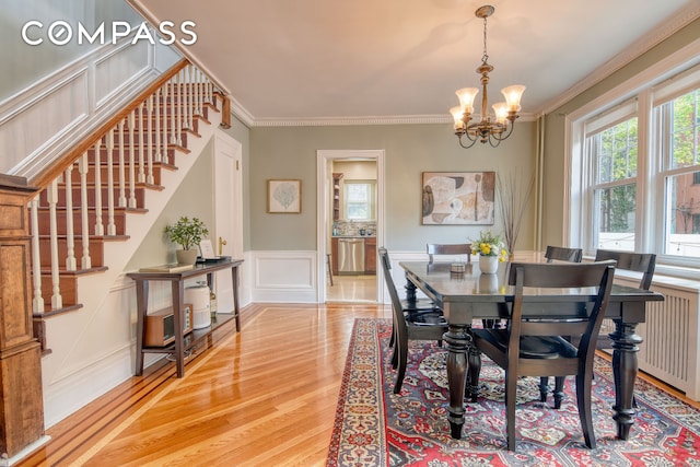 dining space with an inviting chandelier, light wood-style floors, stairs, a decorative wall, and ornamental molding