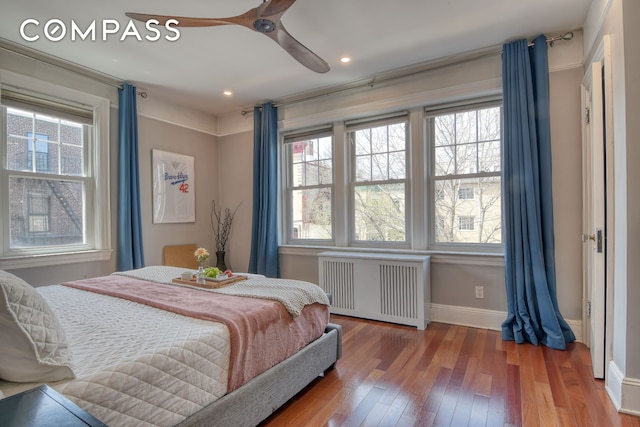 bedroom with radiator, baseboards, wood-type flooring, and multiple windows