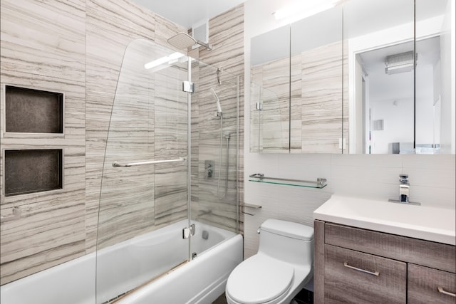 bathroom featuring vanity, enclosed tub / shower combo, toilet, and tile walls