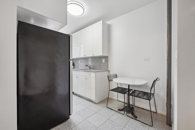 kitchen featuring freestanding refrigerator, tasteful backsplash, a sink, white cabinets, and baseboards