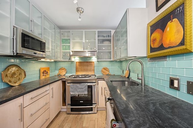 137 E 36th St Unit 11-B, New York City, NY 10016 - kitchen featuring appliances with stainless steel finishes, a sink, light wood finished floors, dark stone countertops, and glass insert cabinets