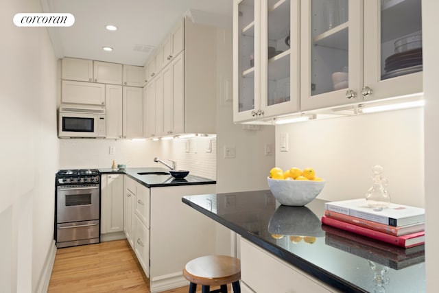 160 E 26th St Unit 5E, New York City, NY 10010 - kitchen featuring stainless steel range with gas cooktop, white microwave, backsplash, white cabinets, and light wood-style flooring