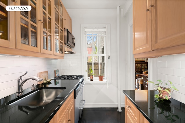 kitchen with a sink, stainless steel appliances, decorative backsplash, dark stone counters, and glass insert cabinets