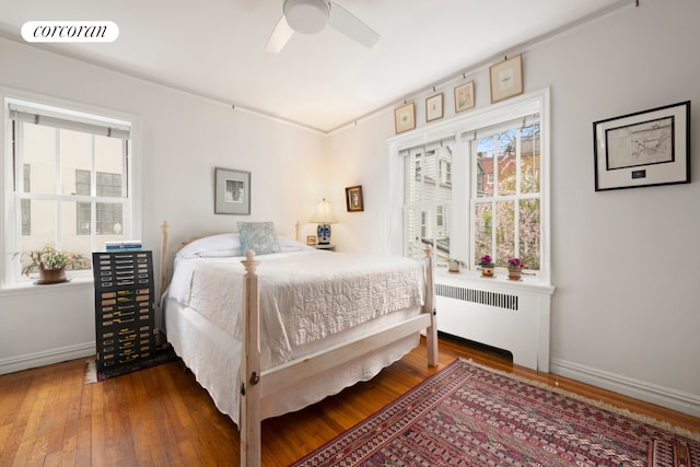 bedroom with radiator heating unit, wood-type flooring, multiple windows, and baseboards