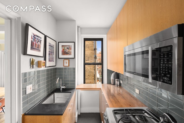 kitchen with stainless steel microwave, gas range, a sink, backsplash, and wood counters