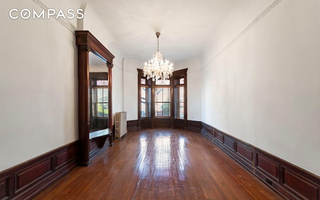 256 Decatur St, New York City, NY 11233 - unfurnished dining area featuring radiator heating unit, a chandelier, wainscoting, a decorative wall, and dark wood finished floors