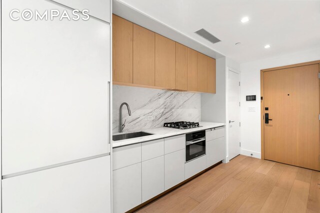 208 Delancey St Unit Gc, New York City, NY 10002 - kitchen featuring wall oven, a sink, light wood-style flooring, backsplash, and light countertops