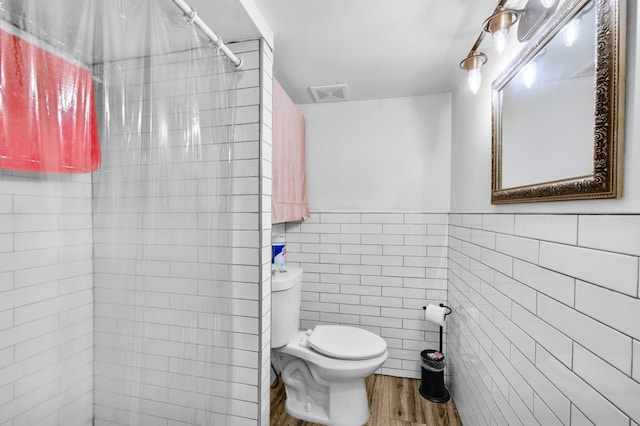 full bath with a tile shower, wood finished floors, visible vents, toilet, and tile walls