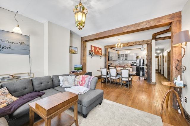 living room featuring beam ceiling, light wood-style flooring, and an inviting chandelier
