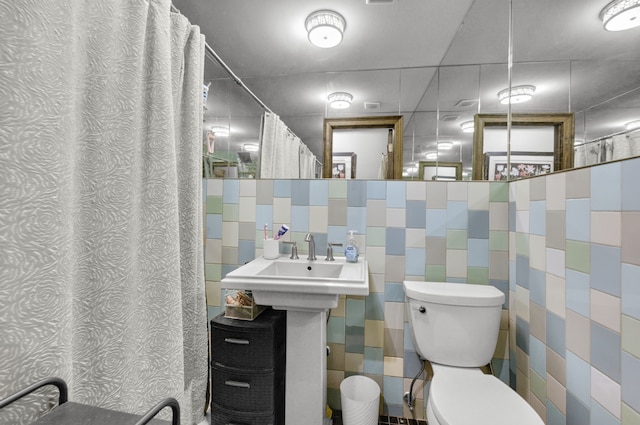 bathroom with curtained shower, tile walls, toilet, and a sink